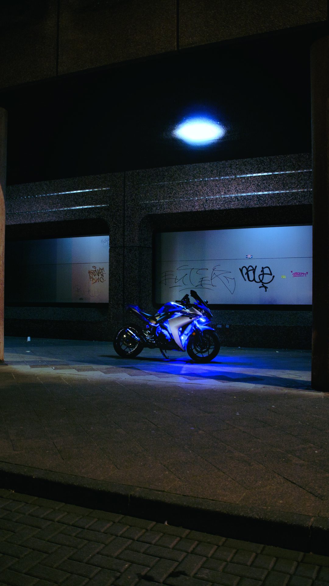 Motorrad bei Nacht mit blauem Licht vor industrieller Fassade.